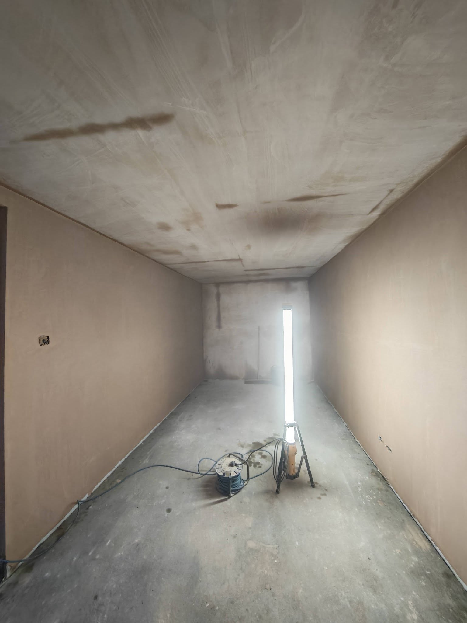 Long room with walls and ceiling freshly skimmed, a work light on the floor