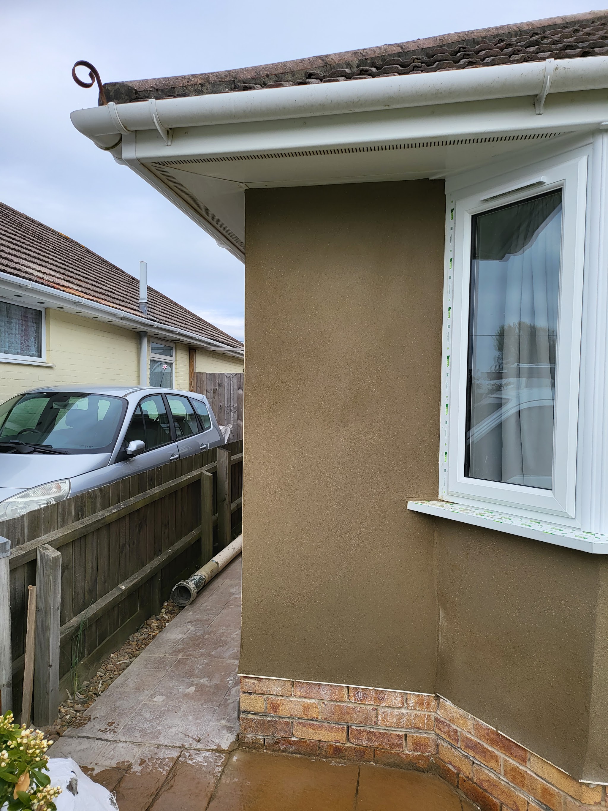 Fresh render on a bungalow corner and bay above a brick plinth